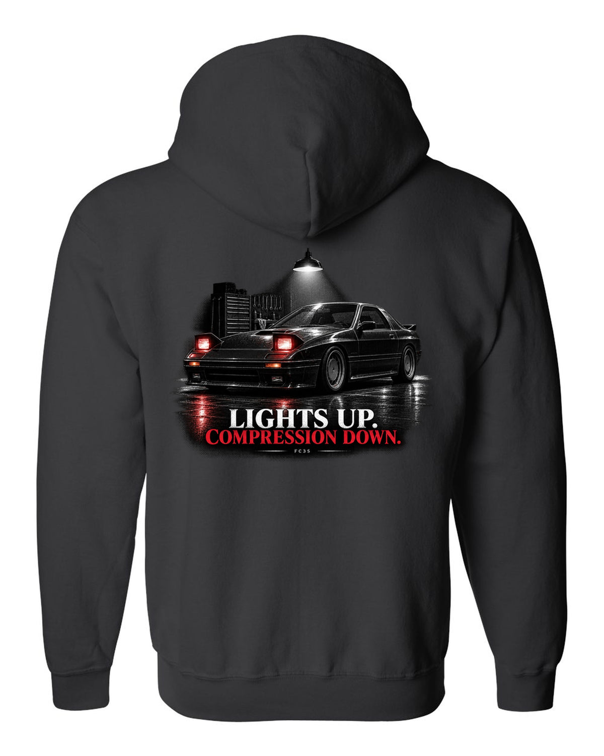 Low front three-quarter Mazda RX-7 FC3S Turbo II in a garage at night black zip hoodie back view with the design